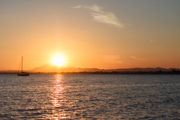 Sailboat sunset fantasy with a silhouetted boat sailing along its journey against a vivid colorful sunset with birds flying in formation against an orange and yellow color filled sky.