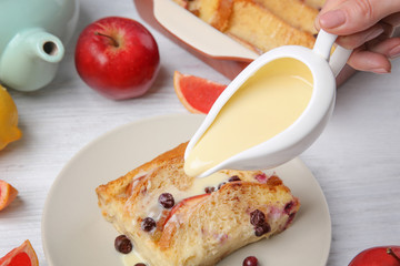 Pouring sauce on tasty bread pudding with berries on table