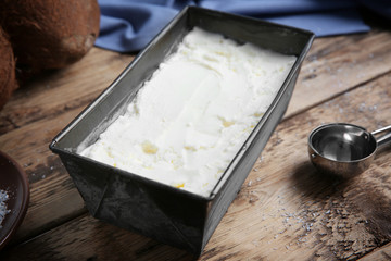 Black container with fresh coconut ice cream on wooden table