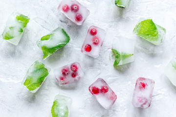 Obraz na płótnie Canvas ice cubes with red berries and mint top view gray stone background