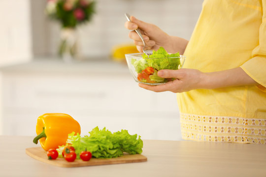 Young pregnant woman eating salad in kitchen