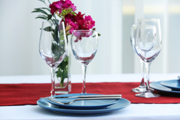 Beautiful festive table setting and vase with flowers in light room