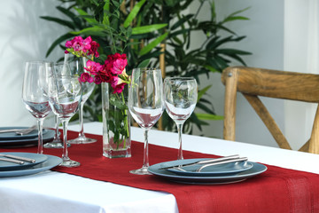 Beautiful festive table setting and vase with flowers in light room