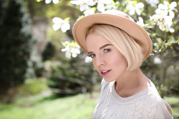 Young blonde girl in hat near blooming magnolia tree