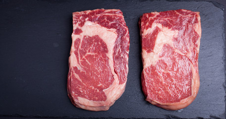 Two fresh raw marble meat, black Angus ribeye steak on a dark stone background.
