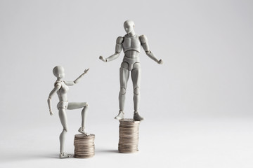 Income inequality concept shown with realistic male and female figurines and piles of coins. Female...