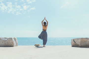 Young woman doing yoga in the beach. Female wearing sport clothes in eagle asana with defocused sea...