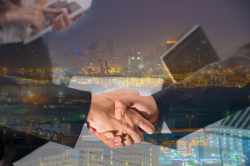 Double Exposure of a businessman handshake on Aerial view of Container port with cityscape at night in Bangkok, Thailand.