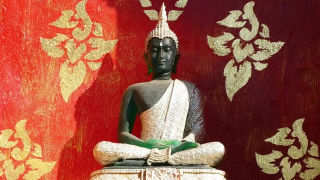 Buddha statue on the background of wall of burgundy color in Buddhist temple.