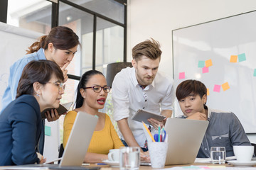 Obraz premium Multiethnic group of happy business people working together, meeting and brainstorming in office using computer, laptop, tablet, and mobile phone.