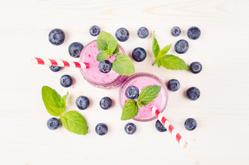 Freshly blended violet blueberry fruit smoothie in glass jars with straw, mint leaves, berries, top view. White wooden board background, copy space.