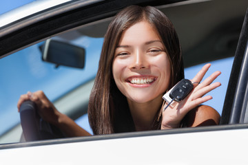 Happy Asian girl teen driver showing new car keys. Young woman smiling driving new car holding key. Interracial ethnic woman driver holding car keys driving rental car.