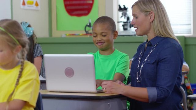 Teacher and student use laptop computer in school classroom