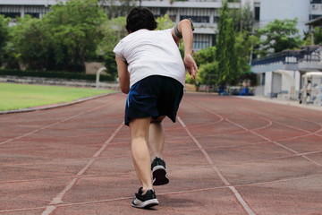 Obraz premium Back view of young Asian sprinter leaving starting on racetrack at athletics stadium.