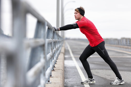 Man runner stretching legs before exercise run outdoors in city urban street during winter. Athlete wearing smartwatch, phone armband for music app and warm gloves, headband, long tights underwear.