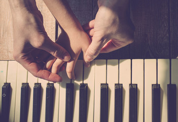 Mother teaches the daughter to play the piano. Concept Mother's Day. Female and children's hands. Vintage toning. Top view
