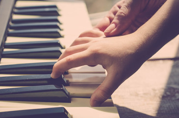 Mother teaches the daughter to play the piano. Concept Mother's Day. Female and children's hands. Vintage toning.