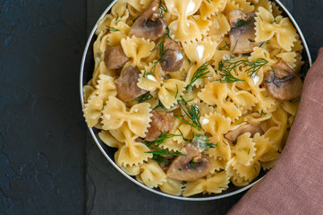 Farfalle pasta in sour cream sauce with mushrooms garnished with dill served in a pan on a black slate background.