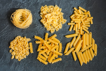 Variety of types of Italian pasta background. Set of raw pasta on a black slate background.