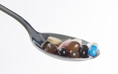 Fototapeta premium Detail view of different pills and capsules in a spoon isolated over a white background.