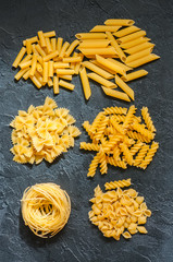 Variety of types of Italian pasta background. Set of raw dry pasta on a black slate background.
