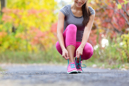 Running shoes woman runner tying shoe lace for run. Happy smiling girl getting ready for jogging lacing run shoe laces. Female sport fitness runner outdoors on forest path in autumn fall season.