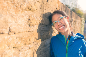 happy smiling young asian teenager girl leaning against stone wall