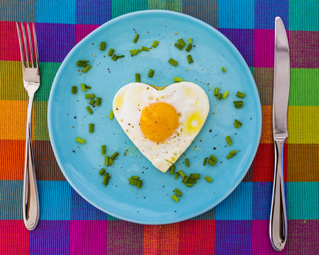 Tasty fried egg in the shape of a heart served on a blue plate.