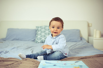 Little boy plays on the bed. A happy little kid.