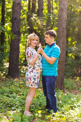 Fototapeta premium Pregnancy, family, happiness and fun concept - Man and pregnant woman have fun with candy in the park