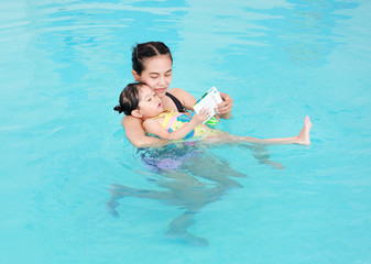 Mother and child swimming in the pool. Happy young woman teaching her daughter to swim.