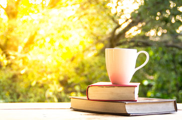 A cup of coffee and book on the wooden table and blurred nature background