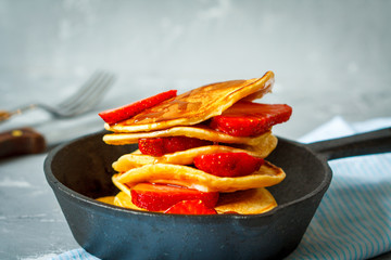 Homemade pancakes with strawberries and syrup on a cast-iron frying pan.