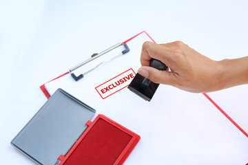 Close-up hand Stamping Exclusive on paper sheet with red Ink pad(box) against white background.