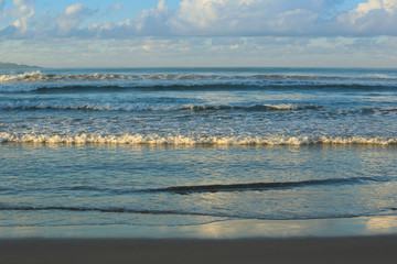 Wave running to the sand beach under blue sky