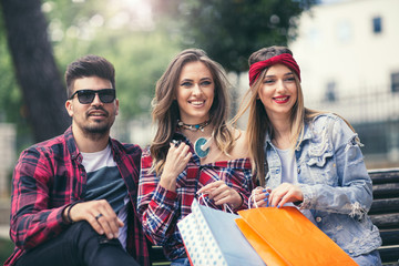 Three friends sitting on a park bench after shopping