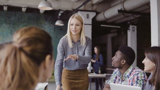 Beautiful Blonde Woman Manager Giving Direction To Multiethnic Team. Creative Business Meeting At Modern Hipster Office.