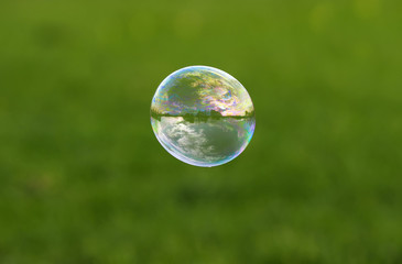 colorful soap bubble with reflection of the landscape flying on a bright summer meadow on a Sunny day