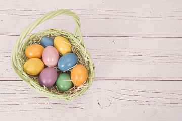Colored eggs in a basket on a pink wooden background with space for text