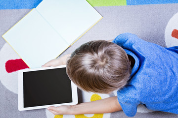 Boy looking at tablet pc, lying on the floor with books