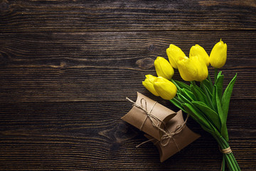 Bouquet of  yellow tulips with gift boxes on dark wooden background.