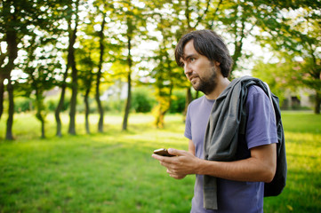 Naklejka na ściany i meble Young bearded guy looks thoughtfully at the screen of the smartphone.