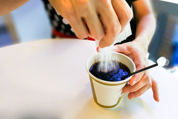 Women pouring sugar granules from sachet into black coffee
