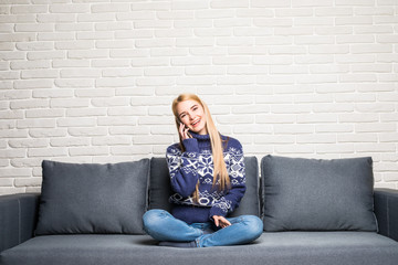 Obraz premium Beautiful young woman talking on the phone at home sitting on the couch.