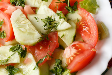 Vegan food, spring salad with tomatoes, cucumbers, parsley and dill on a white table