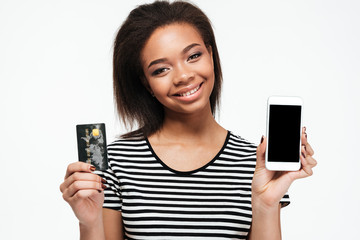 Happy young african lady using phone and holding debit card.