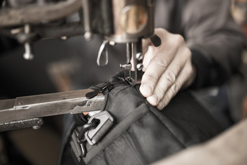 Tailor man sews up a bag in a workshop