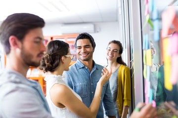 Smiling executives discussing over sticky note on glass wall