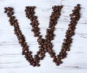 W letter of the English alphabet made of coffee beans. Light, old wooden background. Selective focus.