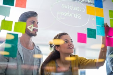 Smiling executives writing on sticky notes on glass wall